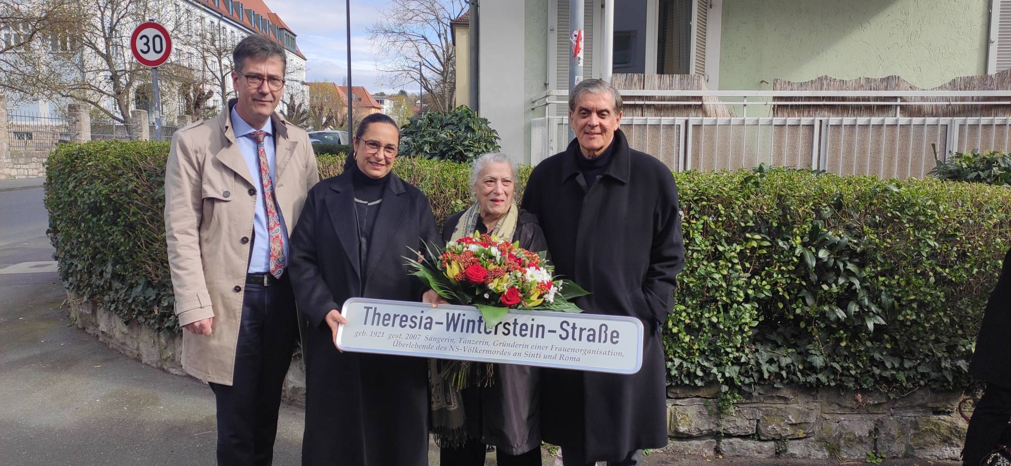 Four persons beneath the newly unveiled street sign.