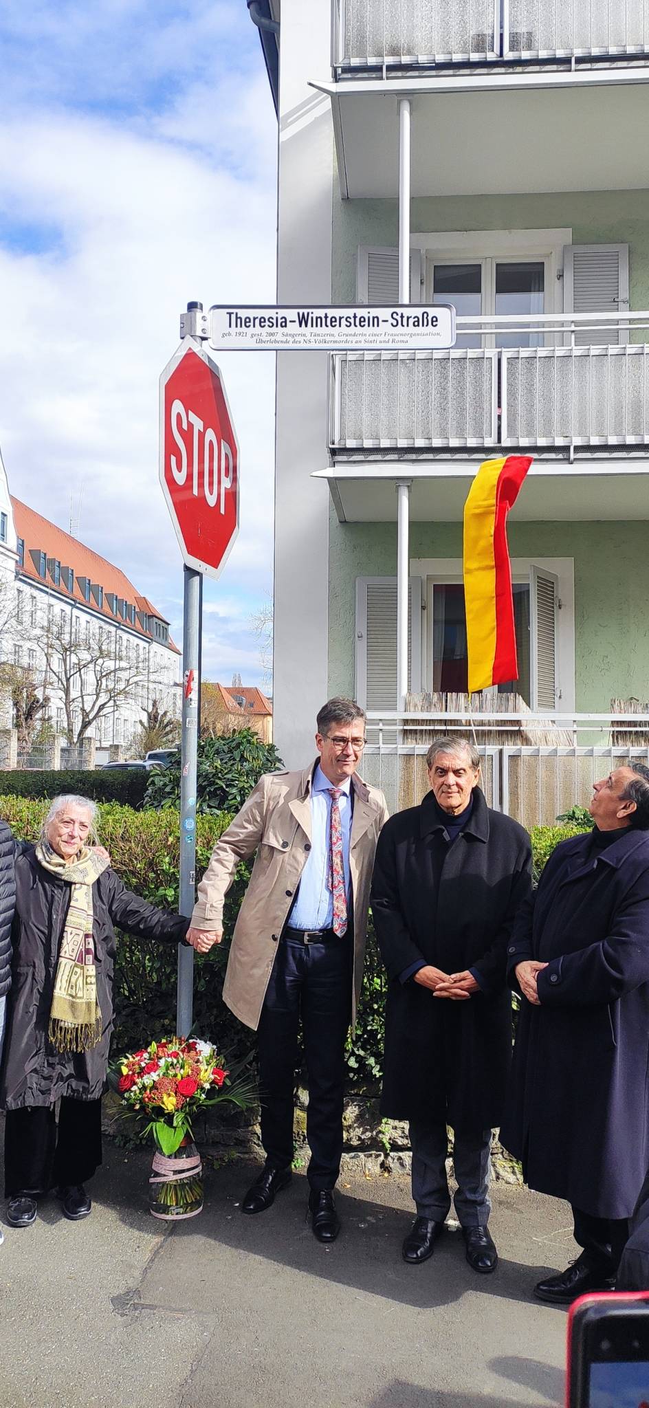 Four persons beneath the newly unveiled street-sign.